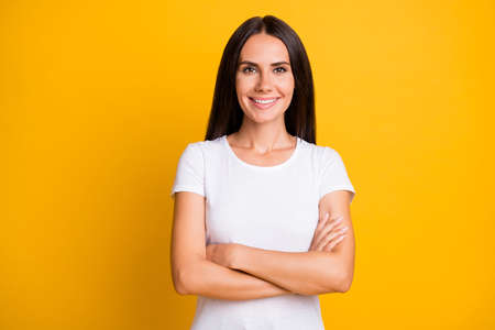 Photo portrait of woman wearing white outfit smiling confident with folded hands isolated on bright yellow color backgroundの写真素材
