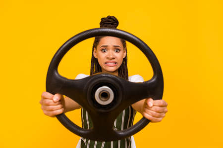 Photo of unhappy scared young afro american woman hold steering wheel isolated on yellow color backgroundの写真素材
