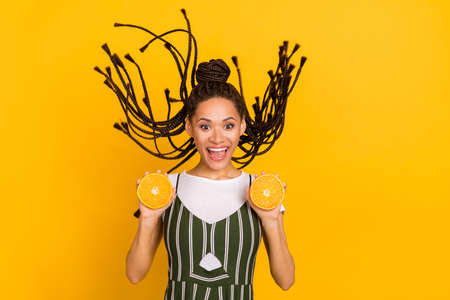 Photo of cheerful young afro american woman hold oranges fly hair wind isolated on yellow color backgroundの写真素材