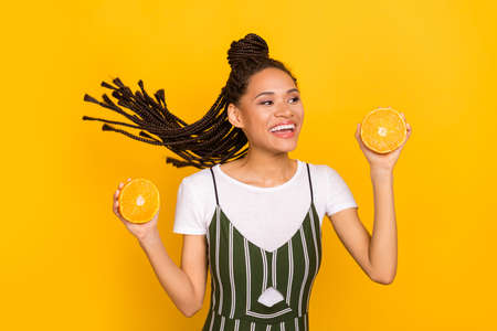 Portrait of attractive cheerful girl having fun holding in hands orange pieces isolated over bright yellow color backgroundの写真素材