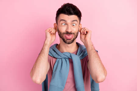 Photo of funky silly young man stick out tongue hold hands ears make funny face isolated on pink...