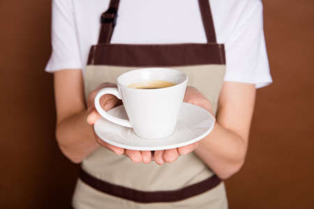 Cropped portrait of waitress arm holding showing fresh coffee cup isolated on brown color backgroundの写真素材