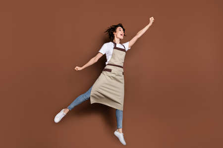 Full size photo of carefree crazy girl raise fist up look empty space open mouth isolated on brown color backgroundの写真素材