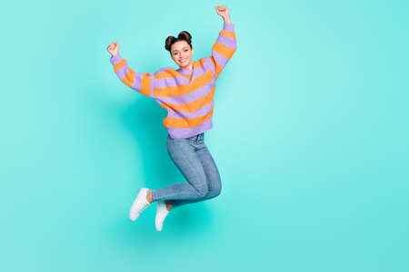 Full length portrait of charming cheerful person jumping fists up celebrate isolated on blue color...