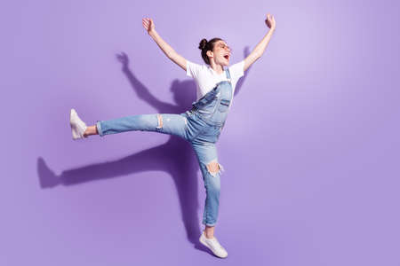Photo of charming shiny young woman dressed denim overall glasses dancing looking empty space isolated purple color backgroundの写真素材