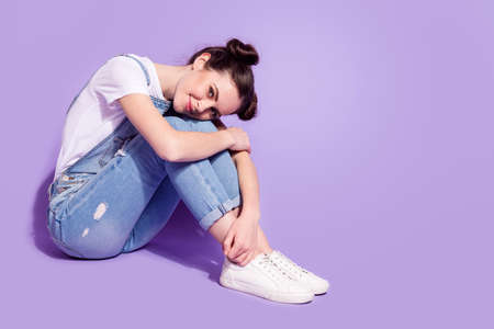 Photo of charming sweet young lady neck wear jeans overall sitting floor having rest empty space isolated violet color backgroundの写真素材
