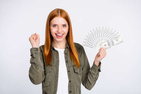 Portrait of attractive cheerful red haired girl holding cash celebrating salary deposit freelance isolated over white light color backgroundの写真素材