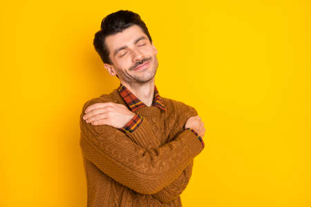 Photo of half turned man closed eyes arms hug shoulder wear sweater isolated on yellow color backgroundの写真素材