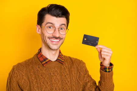 Photo of promoter guy hold credit card beaming smile wear eyewear brown pullover isolated bright...