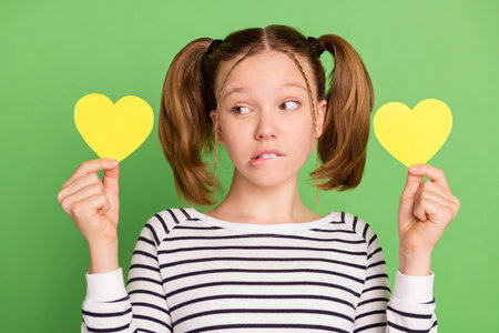Photo of sad blond hairdo small girl look hearts wear striped sweater isolated on green color backgroundの写真素材