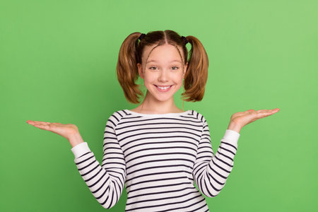 Photo of lovely blond hairdo small girl hold empty space wear striped sweater isolated on green...