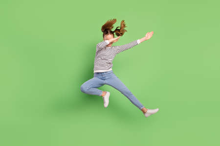 Photo of cute adorable school girl wear white pullover jumping high dancing isolated green color backgroundの写真素材