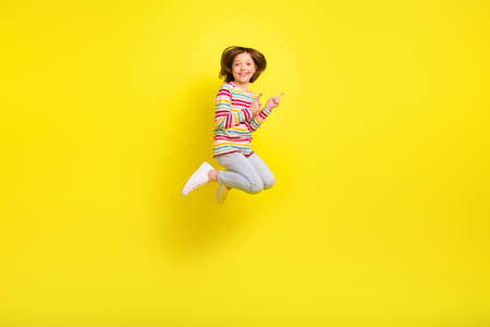 Full body photo of charming cheerful young small girl jump up point finger empty space isolated on yellow color backgroundの写真素材