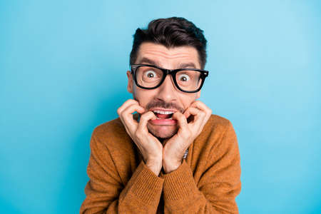 Photo of young man afraid scared bite fingers problem trouble fail nervous isolated over blue color...