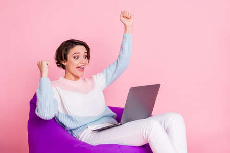 Profile photo of delighted person sitting soft chair look laptop fists up celebrate isolated on pink color backgroundの写真素材