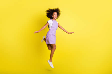 Full length body size view of cheerful carefree wavy-haired girl jumping having fun leisure isolated over bright yellow color backgroundの写真素材
