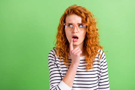 Photo of puzzled shiny young lady dressed striped clothes finger mouth looking empty space isolated green color backgroundの写真素材