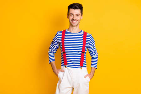 Photo of young attractive handsome smiling cheerful good mood man sailor with hands in pockets isolated on yellow color backgroundの写真素材