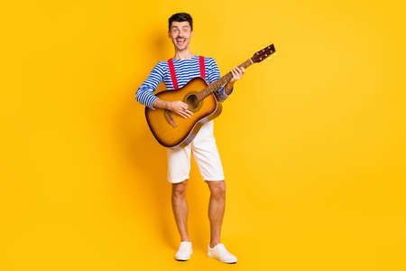 Full size photo of young attractive cheerful positive smiling man playing acoustic guitar isolated on yellow color backgroundの写真素材
