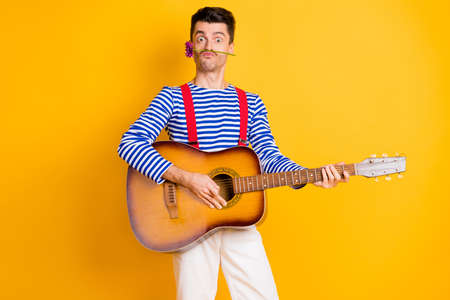 Photo of young funky funny childish comic man with flower above lips playing guitar isolated on...