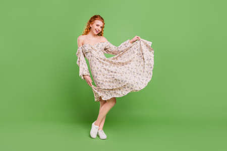 Full body photo of cheerful happy joyful young woman hold hands bottom dress fly isolated on green color backgroundの写真素材