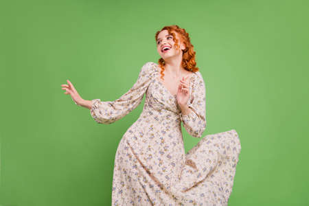 Photo of cheerful positive pretty young woman look empty space fly dress isolated on green color...