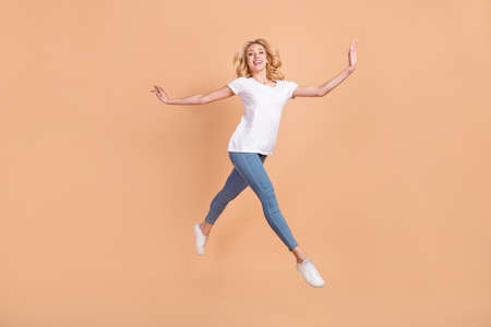 Photo of adorable shiny young lady wear white t-shirt smiling jumping high running isolated beige color backgroundの写真素材