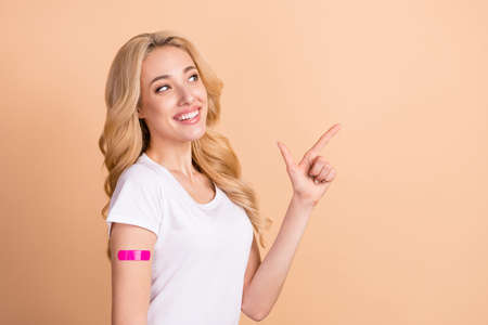 Photo portrait woman smiling with vaccination patch pointing copyspace isolated pastel beige color backgroundの写真素材
