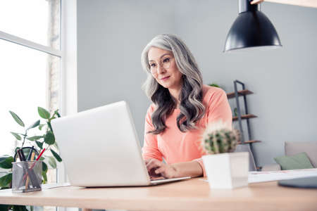 Photo of happy charming old businesswoman sit table look use laptop job office indoors inside house homeの写真素材
