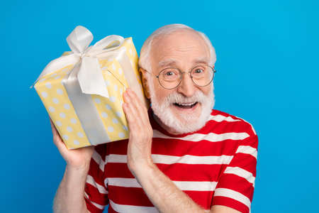 Photo of optimistic old grey hairdo man hold present wear red t-shirt isolated on bright blue color...