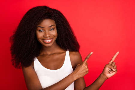 Photo of young african girl happy positive smile point fingers empty space ad promo advise decision isolated over red color backgroundの写真素材