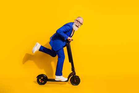 Full size profile side photo of happy smiling good mood mature man riding eco scooter isolated on yellow color backgroundの写真素材