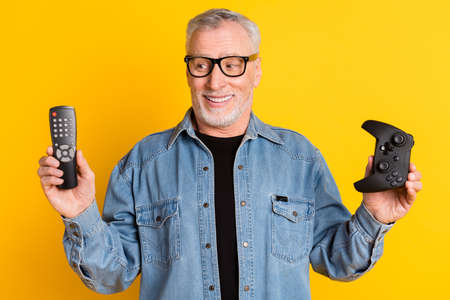 Photo of hooray feel young granddad hold console wear eyewear jeans jacket isolated on yellow color...