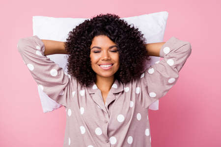 Photo of sweet charming curly dark skin woman dotted nightwear lying white pillow arms behind head...
