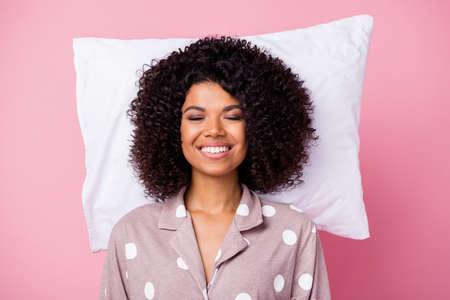 Photo of funny adorable wavy dark skin lady dotted sleepwear lying white pillow isolated pink color backgroundの写真素材