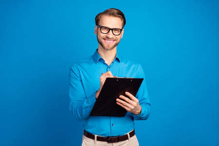 Photo of young cheerful man happy positive smile write to-do list notepad isolated over blue color backgroundの写真素材