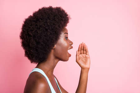 Profile portrait of optimistic brunette curly lady hand talk to empty space wear blue top isolated on pastel pink color backgroundの写真素材