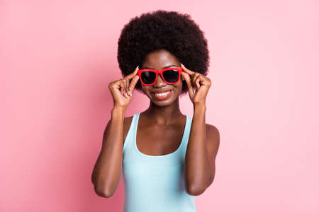 Portrait of optimistic brunette curly lady wear spectacles blue top isolated on pastel pink color backgroundの写真素材