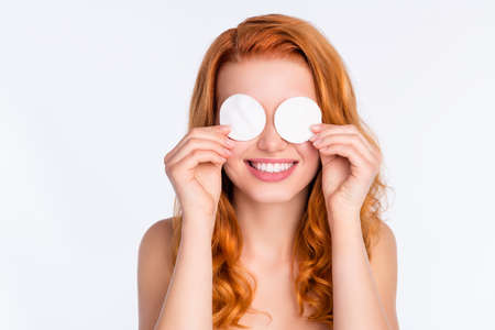 Portrait of young model with curly red hair covered eyes with two cotton disks smilingの写真素材