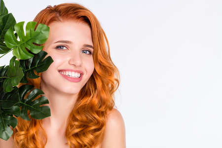 Portrait of pretty girl with curly red hair smiling near green leaves plant