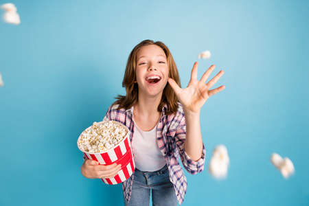 Portrait of positive excited school girl hand throwing popcorn toothy smile look cameraの写真素材