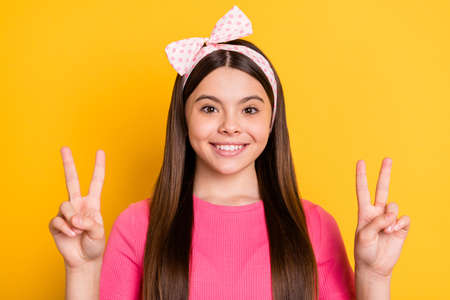 Adorable cute school girl wear pink t-shirt showing two v-signs smiling