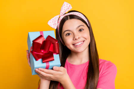 Portrait of cute sweet small schoolgirl dressed pink t-shirt holding present box smiling