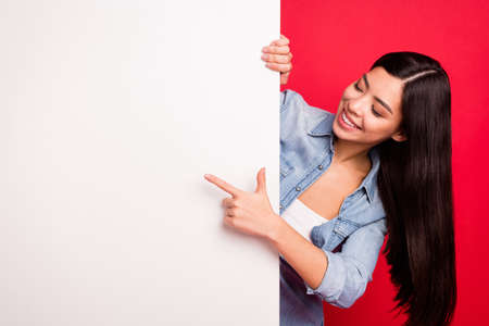 Portrait of attractive cheerful girl demonstrating big blank poster ad promo novelty isolated over bright red color backgroundの写真素材
