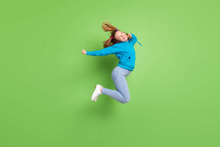 Full body photo of dreamy happy young girl jump up look empty space fly hair isolated on green color backgroundの写真素材