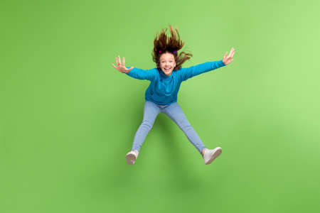 Full body photo of crazy happy excited small girl jump up enjoy weekend fly hair isolated on green color backgroundの写真素材