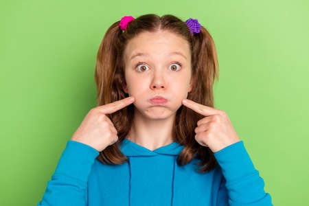 Photo of funky happy nice little girl point fingers cheeks blow air isolated on shine green color...