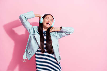 Photo of joyful happy woman stand copyspace closed eyes enjoy music headset isolated on pink color...