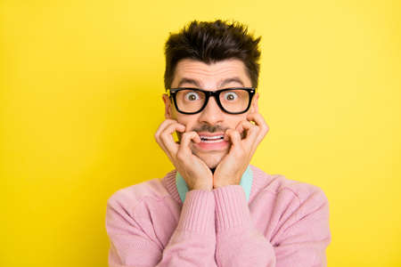 Photo of young handsome afraid scared shocked stressed man in glasses biting fingers isolated on yellow color backgroundの写真素材