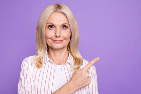 Photo of charming pretty mature woman dressed pink shirt pointing finger empty space isolated purple color backgroundの写真素材